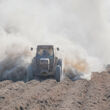 A tractor plowing a field with dust billowing out behind it.