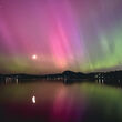 Pink and green northern lights reflect on a bay