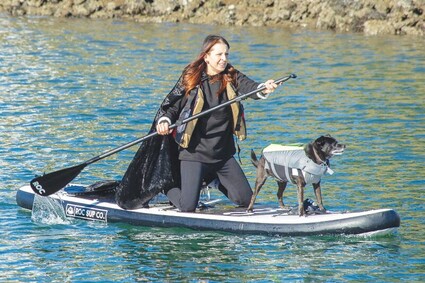 A woman dressed as a witch on a paddleboard with her dog on the front.