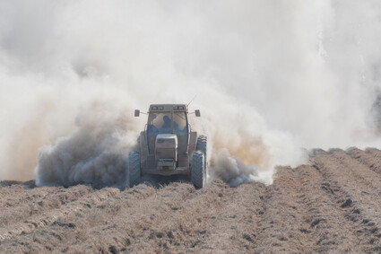 A tractor plowing a field with dust billowing out behind it.