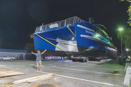 Rigger standing in front of ferry being rolled from parking lot toward barge.