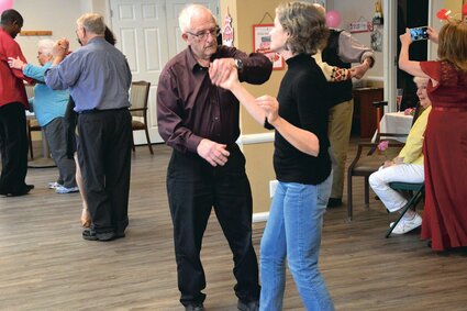 An elderly man dances with his middle-aged adult daughter
