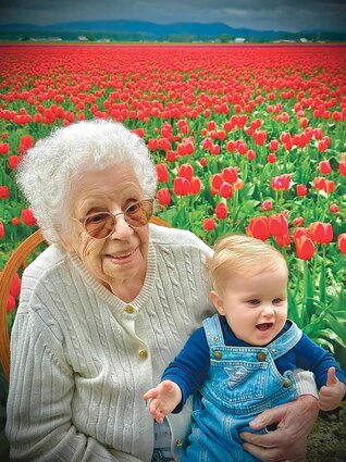 An elderly woman sits with a young relative in a blooming tulip field