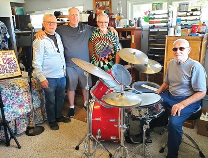 Four musicians gather around a drum kit