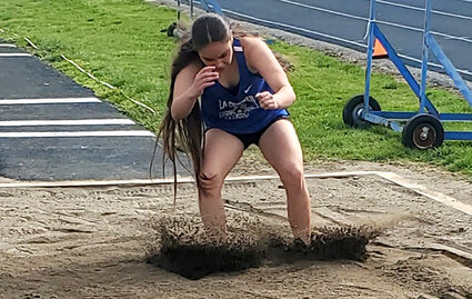 A girl lands the triple jump in the sand