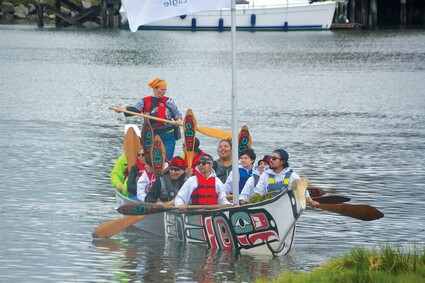 A group of Native American paddlers arrive in a traditional canoe